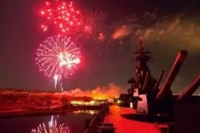 Red fireworks over a ship deck with visible cannons at night.