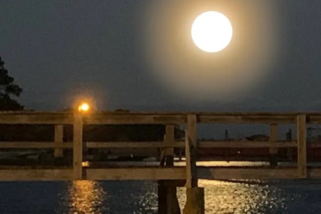 Full moon shining over water with a wooden bridge silhouette.