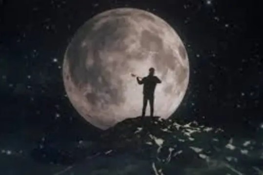 Person standing on hill playing violin with full moon in the background.