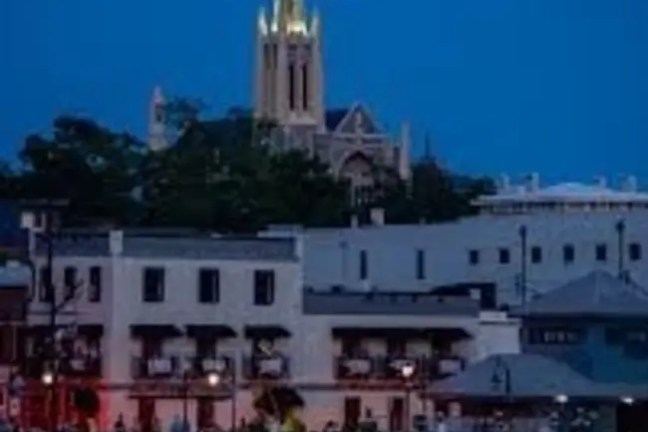 Bright full moon above a church steeple, with a waterfront town in foreground at dusk.