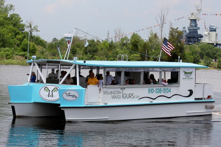 Blue and white tour boat on river with passengers and American flag.